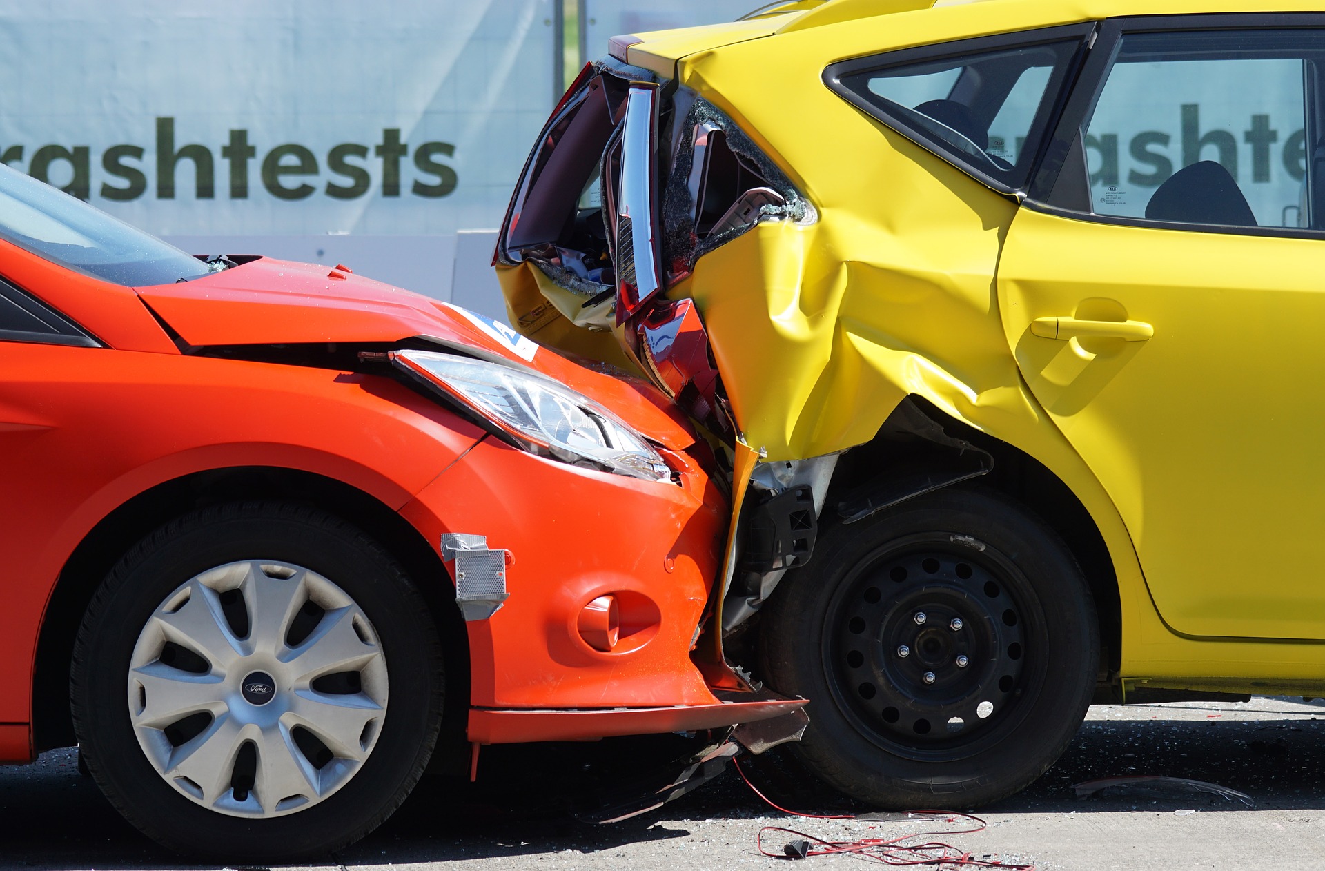 An orange car crashing into the rear of a yellow car which has crumpled under the impact.