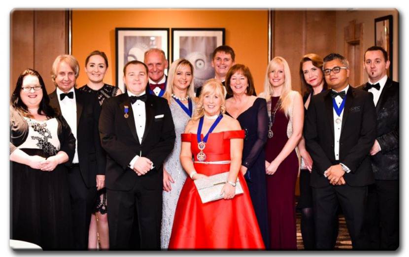 A photo from the CII Ball. Viv can be seen at the front in a vibrant red dress, sporting the President medallion. Other attendees gather around in black formal dresswear.