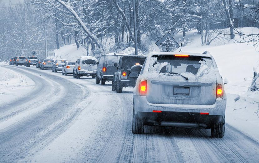 Tailbacks of traffic along a heavily snowed over road; snowbanks line the sides, with snow covered trees overhanging.