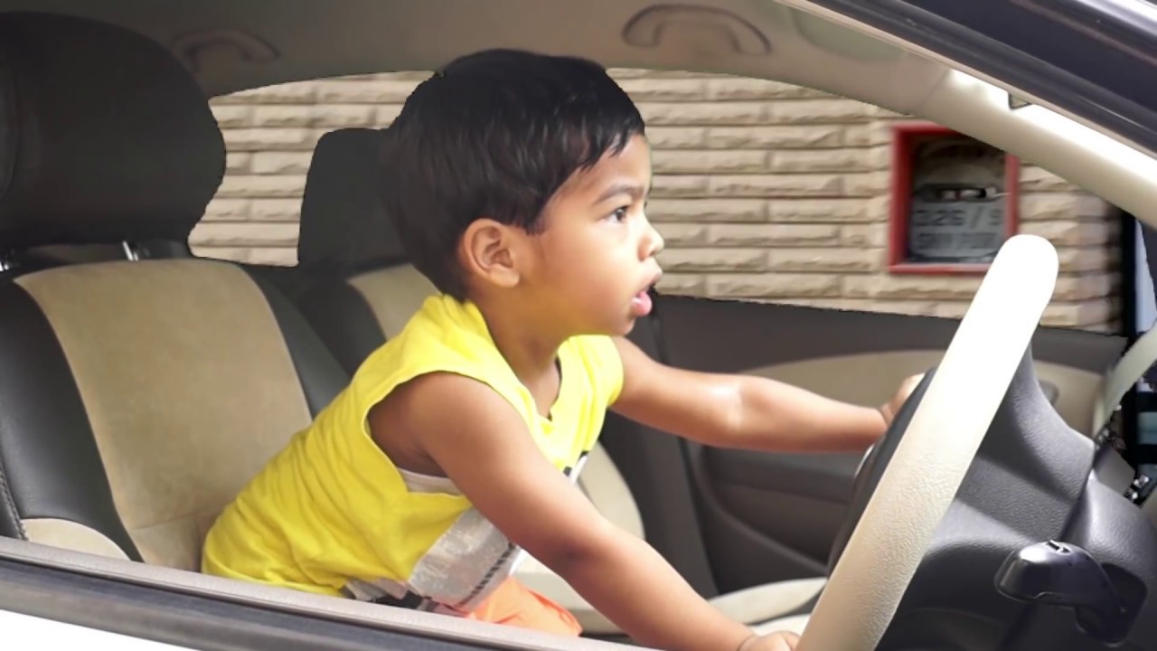 A young child standing on the drivers seat of a vehicle, clutching to the steering wheel as he gazes through the windscreen.