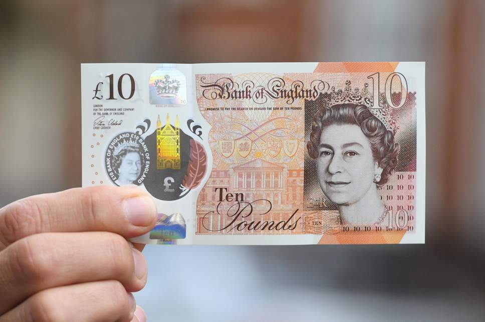 A hand holding up the new polymer ten pound note between pinched finger and thumb, against a blurred out background.