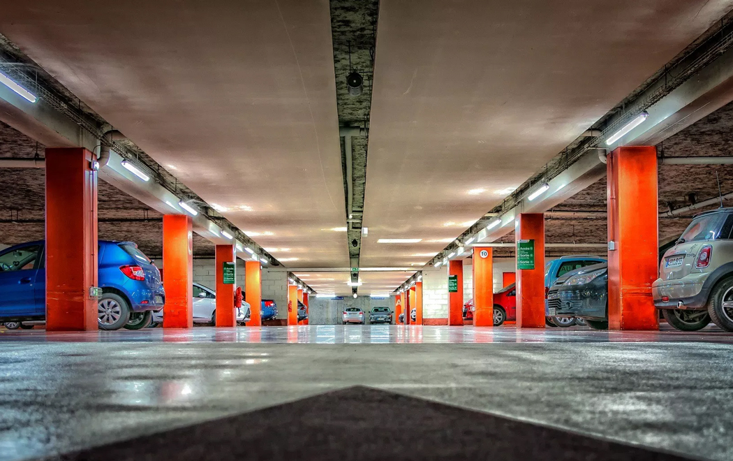 The picture is taken from ground level, looking up across a multistory car park; orange pillars support the ceiling, and a range of different vehicles occupy the parking bays.