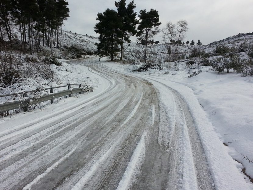 A winding road in the middle of snow covered terrain, with a visibly dangerous road surface that is heavily iced and snow covered.